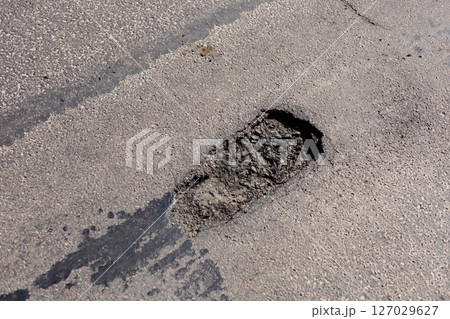 A large pothole is present on an asphalt road, creating obstacles for vehicles in a residential neighborhood during the daytime A large pothole is present on an asphalt road, creating obstacles for vehicles in a residential neighborhood during the daytime 127029627