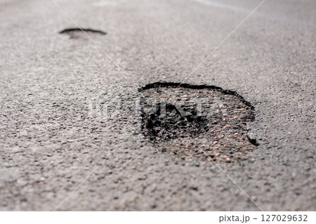 Potholes are visible on a city street, highlighting the urgent need for road repairs to ensure safety for vehicles and pedestrians 127029632