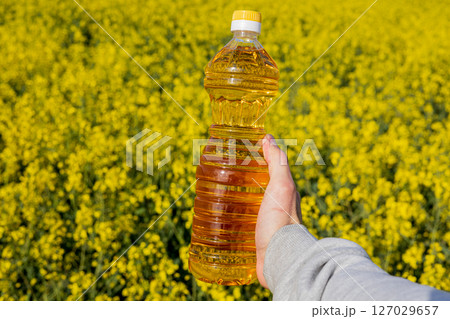A person holds a bottle of canola oil against the vibrant yellow backdrop of a rapeseed field, highlighting agricultural growth 127029657