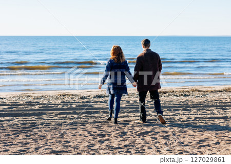 Loving couple walks on beach along sea on sunny autumn day. Weekend and lifestyle concept. Back view. High quality photo 127029861