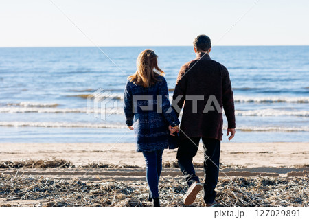 Loving couple walks on beach along sea on sunny autumn day. Weekend and lifestyle concept. Back view. High quality photo Loving couple walks on beach along sea on sunny autumn day. Weekend and lifestyle concept. Back view. High quality photo 127029891