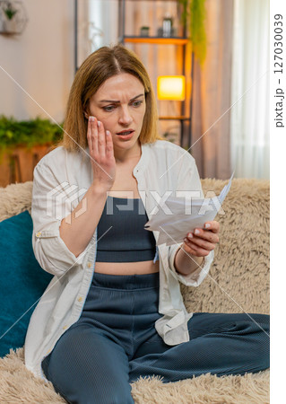 Adult woman reacting to financial stress at home reading utility bills sad worried expression stress Adult woman reacting to financial stress at home reading utility bills sad worried expression stress 127030039