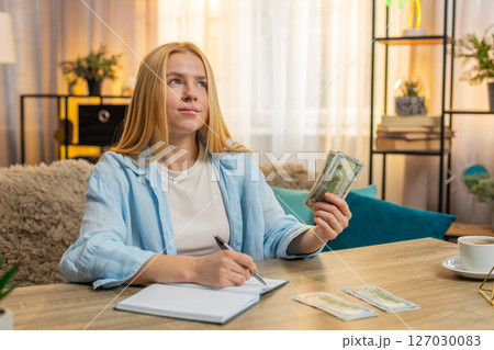 Young woman organizing expenses at home, counting money cash banknotes, writing notes, happy focus Young woman organizing expenses at home, counting money cash banknotes, writing notes, happy focus 127030083