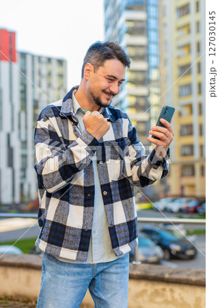Happy young man using smartphone celebrating victory win good message news on downtown city street 127030145