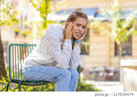 Displeased woman rubbing temples to cure headache problem suffering from migraine stress on street Displeased woman rubbing temples to cure headache problem suffering from migraine stress on street 127030474