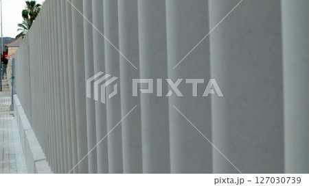 A new relief concrete fence stands tall, displaying its textured surface and vertical lines. A new relief concrete fence stands tall, displaying its textured surface and vertical lines. 127030739