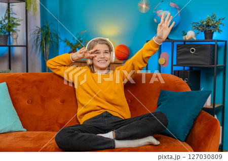 Teenager boy dancing on sofa at home with wireless headphones, enjoying music, moving to rhythm 127030809