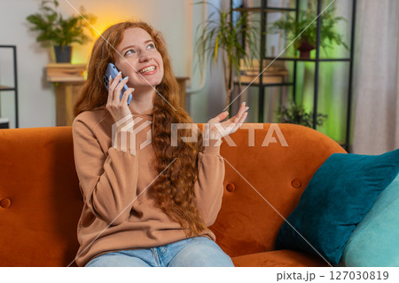 Smiling young Caucasian woman making phone conversation with friends sitting on sofa couch at home Smiling young Caucasian woman making phone conversation with friends sitting on sofa couch at home 127030819