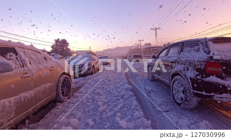 Cars covered in snow are parked on a snow-filled street at sunset. Concept of winter weather and urban life. 127030996
