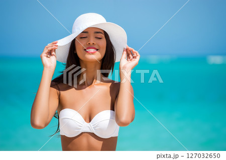Young Woman Enjoying a Sunny Day at the Beach Wearing a White Hat and Bikini 127032650