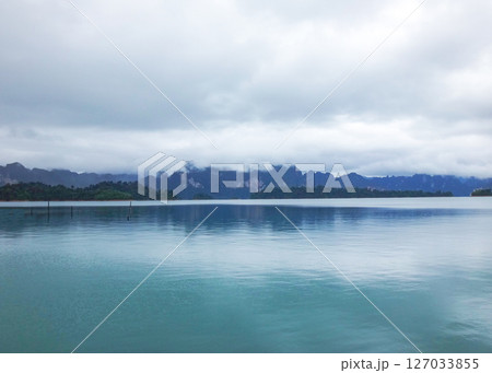 Tranquil Lake Vista: Capturing the serenity of a misty lake, surrounded by the majestic mountains and under a cloudy sky. The still waters reflect the atmospheric conditions. Tranquil Lake Vista: Capturing the serenity of a misty lake, surrounded by the majestic mountains and under a cloudy sky. The still waters reflect the atmospheric conditions. 127033855