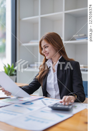 Attractive woman reviews financial documents and calculates figures at desk. Attractive woman reviews financial documents and calculates figures at desk. 127036374