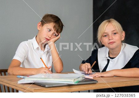 Students Bored Classroom Homework - Two bored students doing their homework in a classroom. 127038365