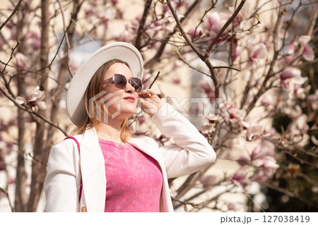 Magnolia Woman Spring: Woman adjusts sunglasses in spring, enjoying flowering magnolia tree during daytime. 127038419