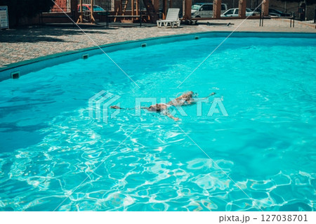 A woman is swimming in a pool. The pool is surrounded by a fence and has a playground in the background. A woman is swimming in a pool. The pool is surrounded by a fence and has a playground in the background. 127038701