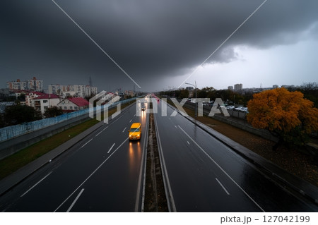 Dark clouds gather over a rainy highway with cars driving through an urban landscape 127042199