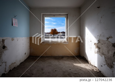 View of a deserted room with an open window overlooking a scenic landscape during daylight 127042236