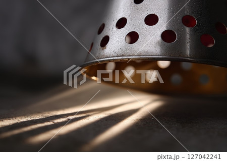 Metal colander casts unique shadows on a textured surface during afternoon light 127042241