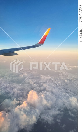 Airplane Wing High Above White Fluffy Clouds at Sunset. View From Plane Window During Flight. Airplane Wing High Above White Fluffy Clouds at Sunset. View From Plane Window During Flight. 127042277