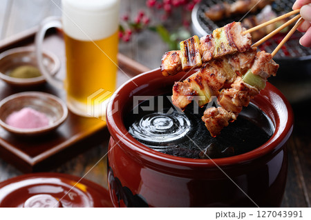炭火焼き鳥をタレにくぐらせる臨場感ある料理写真 127043991