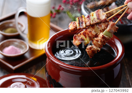 炭火焼き鳥をタレにくぐらせる臨場感ある料理写真 127043992