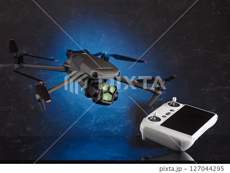 Drone and remote control. Drone hovering in the air. Helicopter with three cameras. Flying device above the ground. Control the flying device. 127044295