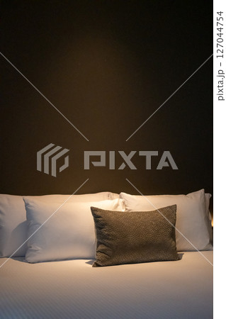 A neatly made hotel bed with soft pillows with warm reading light 127044754