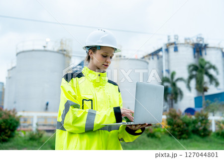 One petrochemical or gas factory worker or technician woman hold laptop for working with smiling in front of the factory. One petrochemical or gas factory worker or technician woman hold laptop for working with smiling in front of the factory. 127044801