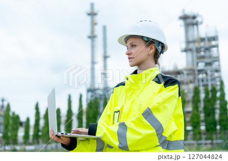 Petrochemical woman worker stand with arm-crossed in front of factory and she look to her right side with smiling. Petrochemical woman worker stand with arm-crossed in front of factory and she look to her right side with smiling. 127044824