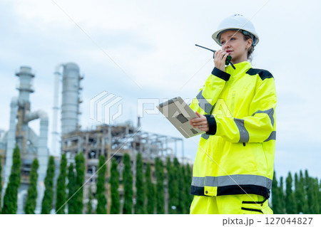 Petrochemical worker or technician woman hold laptop use walkie talkie to contact coworker and stay in front of the factory. 127044827