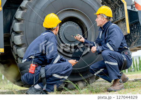 Two factory workers sit near wheel of truck and check or maintenance in workplace area. Two factory workers sit near wheel of truck and check or maintenance in workplace area. 127044829