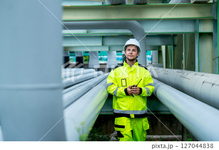 One gas or petrochemical worker man or engineer stand between pipeline in factory workplace and look at camera during work. One gas or petrochemical worker man or engineer stand between pipeline in factory workplace and look at camera during work. 127044838