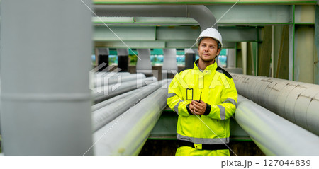 Petrochemical worker man or engineer stand between pipeline in factory workplace and look at camera during work. Petrochemical worker man or engineer stand between pipeline in factory workplace and look at camera during work. 127044839