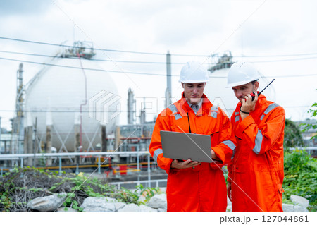 One engineer or gas factory worker use walkie-talkie to discuss with coworker and also use data in laptop to work and stay in front of gas factory tank in workplace. One engineer or gas factory worker use walkie-talkie to discuss with coworker and also use data in laptop to work and stay in front of gas factory tank in workplace. 127044861
