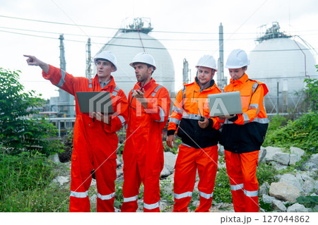 Group of gas factory technicians or engineers with one hold laptop and other one point to his right side and discuss together about their work and stay in front of tank with day light. Group of gas factory technicians or engineers with one hold laptop and other one point to his right side and discuss together about their work and stay in front of tank with day light. 127044862