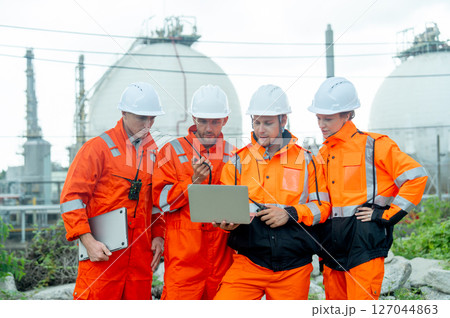 Group of gas factory technicians or engineers with one hold laptop and discuss together about their work and stay in front of tank with day light. Group of gas factory technicians or engineers with one hold laptop and discuss together about their work and stay in front of tank with day light. 127044863
