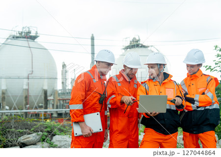 Gas factory workers or engineers with one hold laptop and discuss together about their work and stay in front of tank with day light. Gas factory workers or engineers with one hold laptop and discuss together about their work and stay in front of tank with day light. 127044864