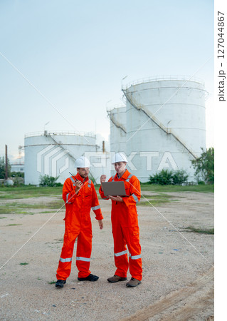 Vertical image of two engineers or gas factory workers discuss together using laptop in front of gas or petrochemical tank in workplace. Vertical image of two engineers or gas factory workers discuss together using laptop in front of gas or petrochemical tank in workplace. 127044867