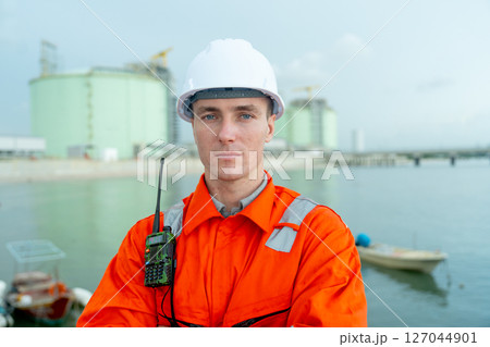 Portrait of petrochemical worker or engineer stand with arm-crossed in front of factory tank. 127044901