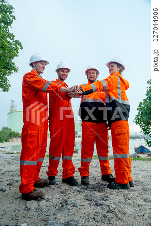 Vertical image of group petrochemical workers or technicians stand and hold hands together in front of factory tank. Vertical image of group petrochemical workers or technicians stand and hold hands together in front of factory tank. 127044906