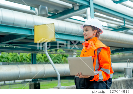 One petrochemical or gas factory worker or technician woman man work using laptop and stand near pipeline in factory workplace. One petrochemical or gas factory worker or technician woman man work using laptop and stand near pipeline in factory workplace. 127044915