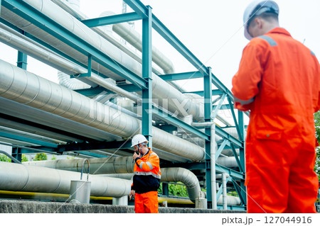 Two petrochemical or gas factory workers or engineers work together near pipeline in factory workplace. 127044916