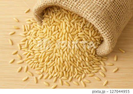 Golden Rice Grains Overflowing Rustic Jute Sack Close-Up Bright Food Macro 127044955