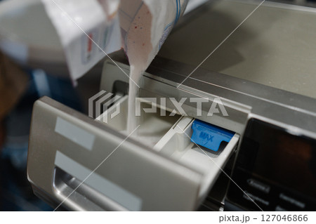 Close-up view of washing powder pouring into detergent drawer of washing machine, setting stage for efficient laundry routine in modern bathroom environment. Concept of cleanliness and housekeeping. 127046866