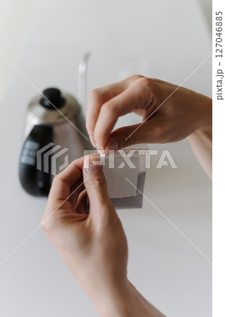 Close-up vertical cropped shot of male hands opening single-serve drip coffee bag, preparing to brew fresh cup of coffee with modern method at home in morning. Process of making freshly brewed coffee. Close-up vertical cropped shot of male hands opening single-serve drip coffee bag, preparing to brew fresh cup of coffee with modern method at home in morning. Process of making freshly brewed coffee. 127046885