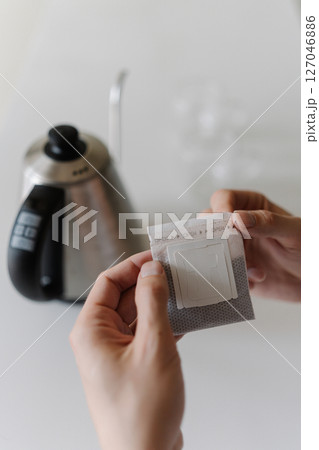Vertical cropped shot of male hands opening single-serve drip coffee bag, preparing to brew fresh cup of coffee with modern method at home in morning, close-up. Process of making freshly brewed coffee Vertical cropped shot of male hands opening single-serve drip coffee bag, preparing to brew fresh cup of coffee with modern method at home in morning, close-up. Process of making freshly brewed coffee 127046886