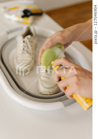 Close-up male hands cleaning pair of dirty white shoes in foldable basin using brush and cleaning foam, taking care of footwear hygiene and maintenance, closeup. Leather footwear care concept. 127046904