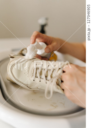 Person applying foam cleaner to dirty white shoe in basin, concentrating on effective shoe care and maintenance while tackling stubborn dirt and grime, close-up. Concept of shoe hygiene. 127046905
