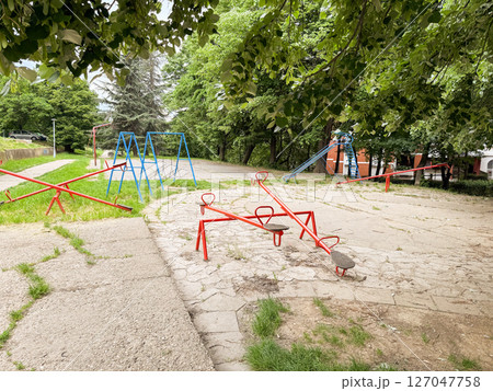 Empty retro playground with seesaws, swings, and a slide under green trees. A quiet and nostalgic public space in the city. Empty retro playground with seesaws, swings, and a slide under green trees. A quiet and nostalgic public space in the city. 127047758