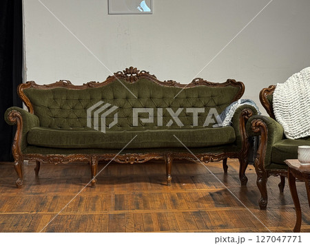 Vintage green velvet sofa with carved wooden frame in cozy interior. Classic furniture style evokes elegance and historical charm 127047771